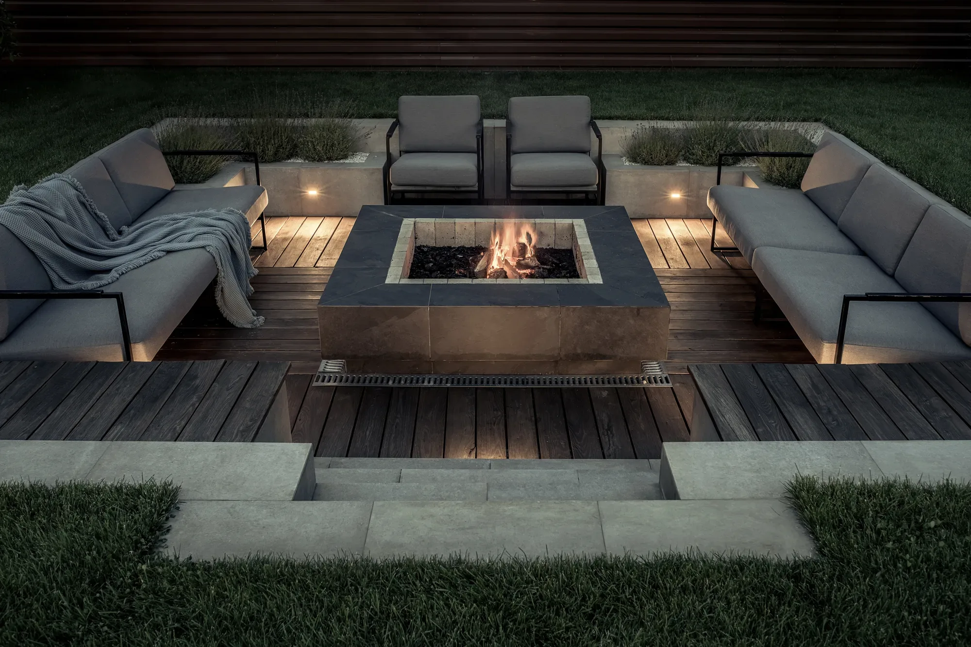 Sunken fire-pit lounge with a stone-clad fire table at night