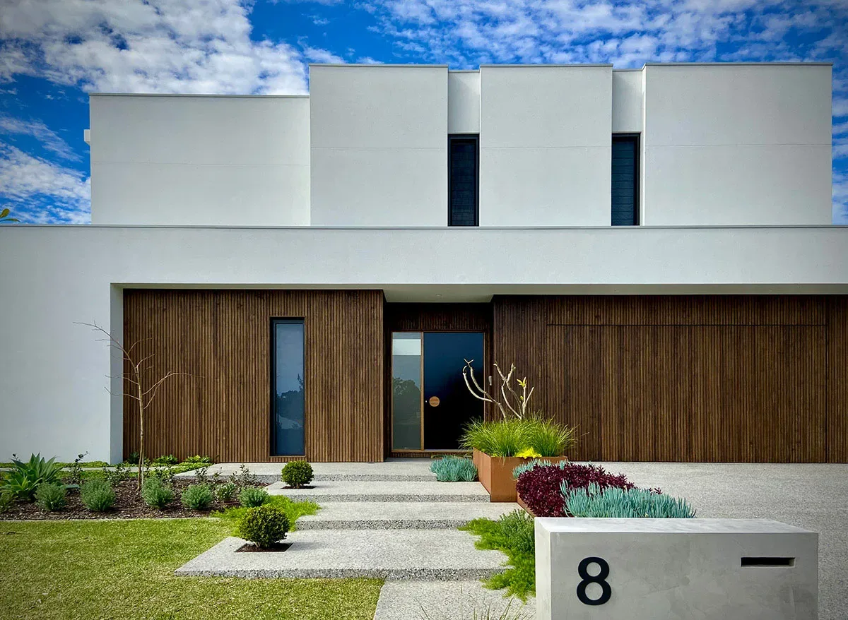 Modern white rendered home entrance with structural garden bed planting at dusk