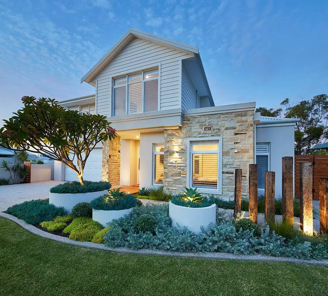 In-ground pool with sandstone paving and landscaped garden beds surrounding the pool area at dusk