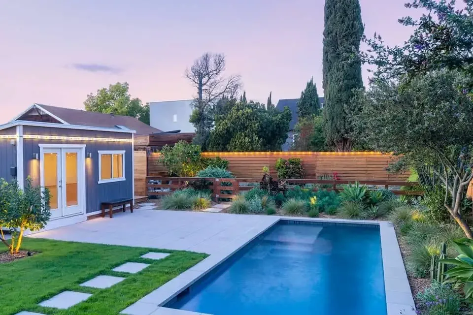 Backyard in-ground pool with sandstone paving surround at dusk