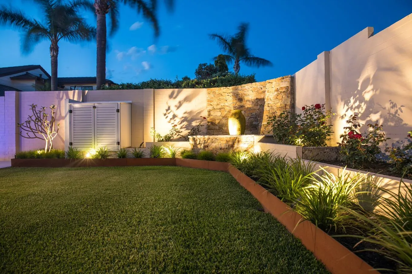 Curved rendered retaining wall with a stacked-stone water feature insert at night