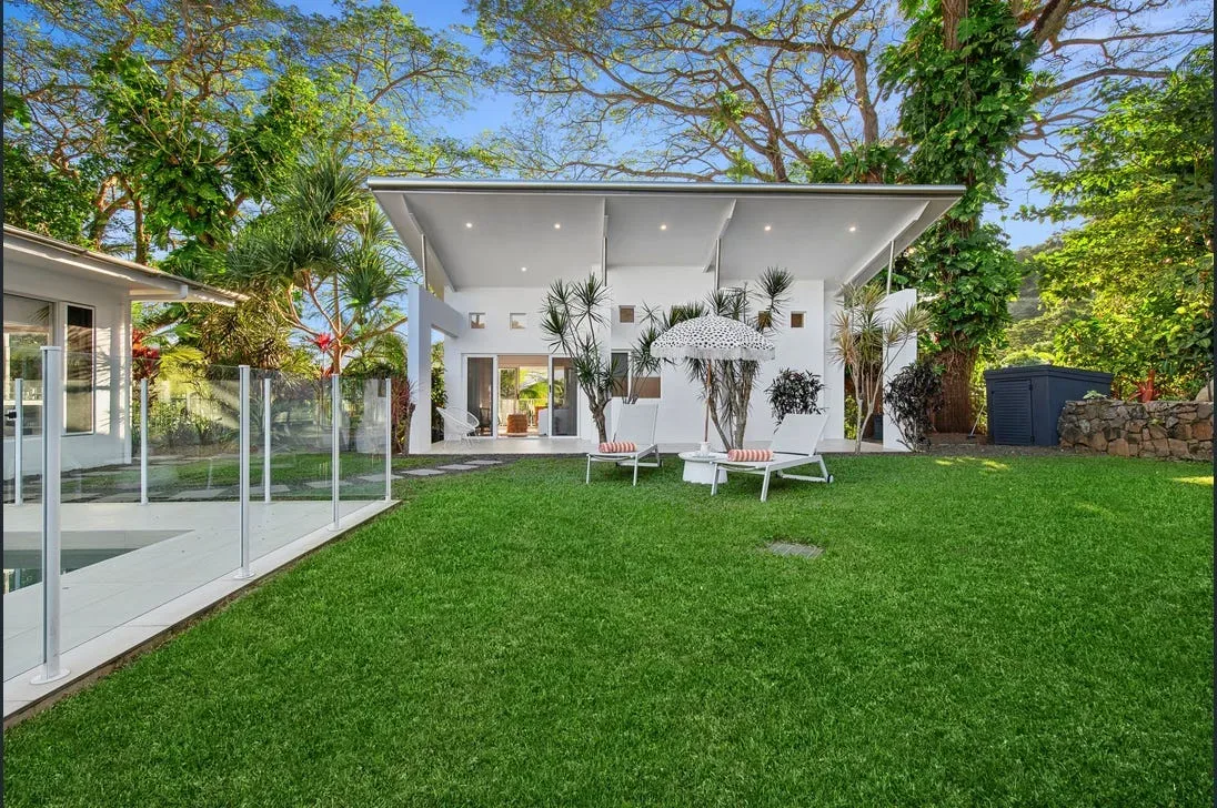 Glass pool fence and edge of an in-ground pool beside a lawn with sun loungers and umbrella
