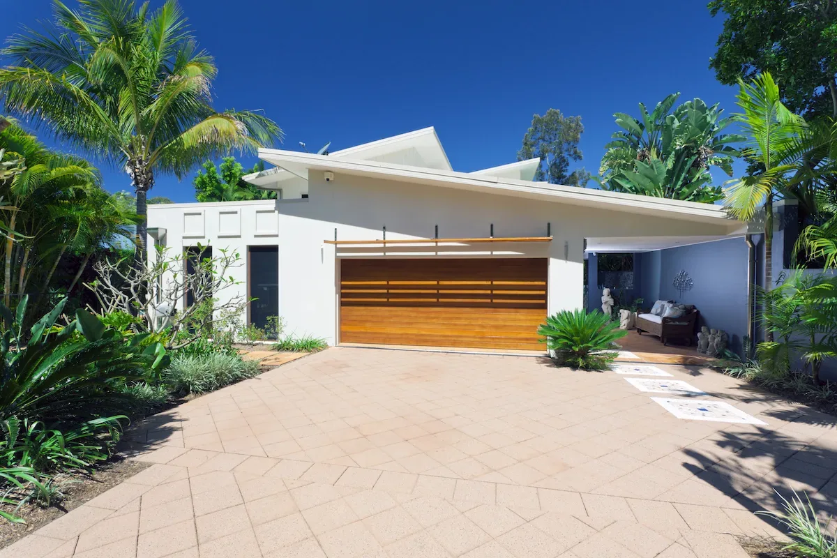Paved courtyard driveway with mature palms, cycads and garden statues in front of a modern house