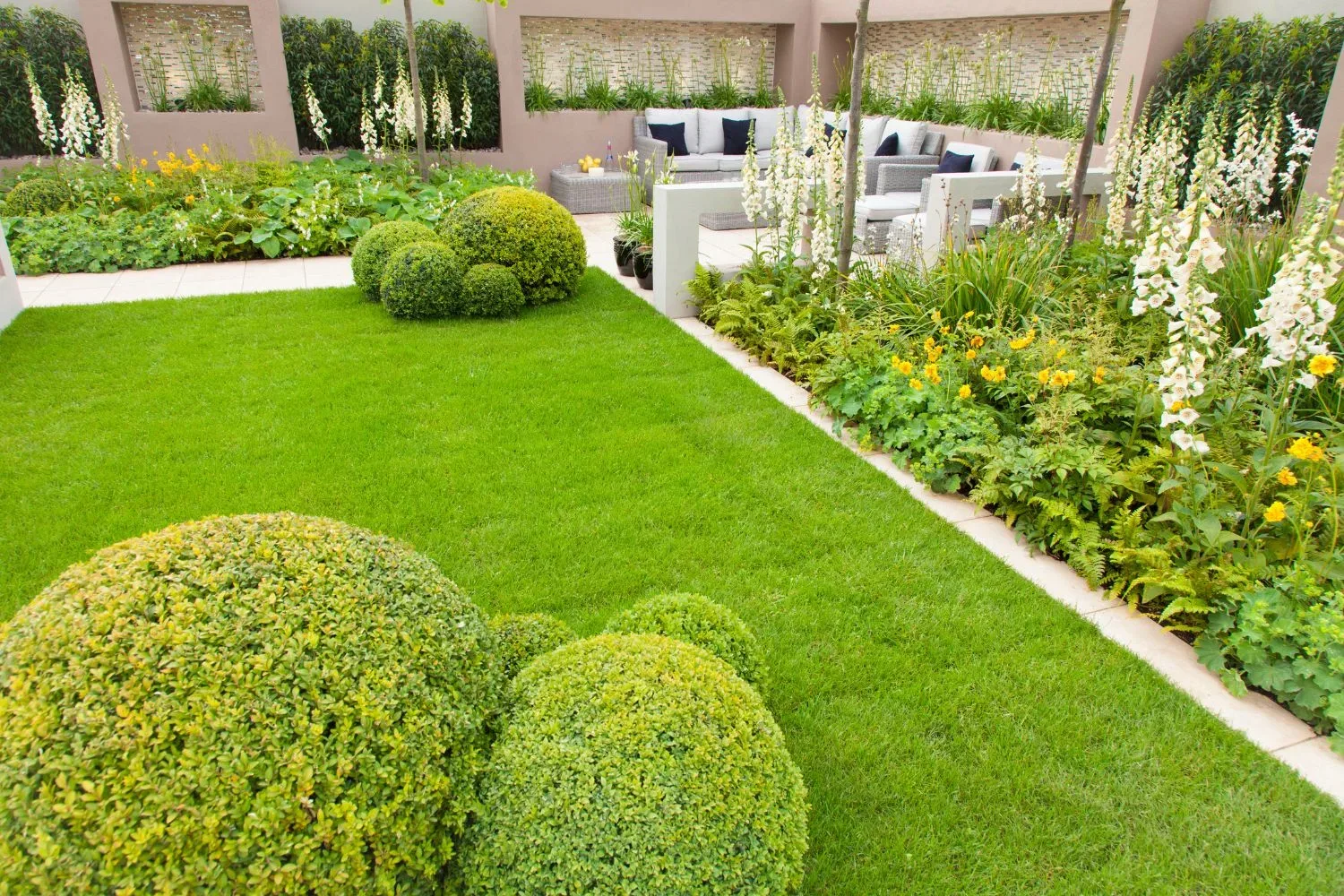 Manicured courtyard lawn with clipped box-hedge topiary and a paved patio lounge area